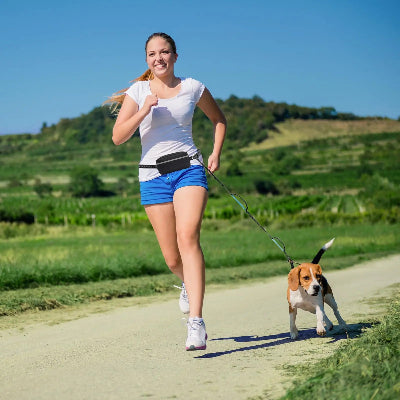 femme sportive court avec son chien attache avec une laisse chien main libre dans une nature verdoyante colline et ciel bleu en arriere plan