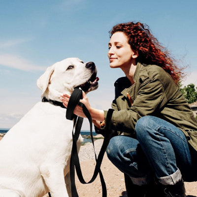 une femme accroupie caresse son chien tenu par une laisse pour chiens noire ciel bleu en arriere plan